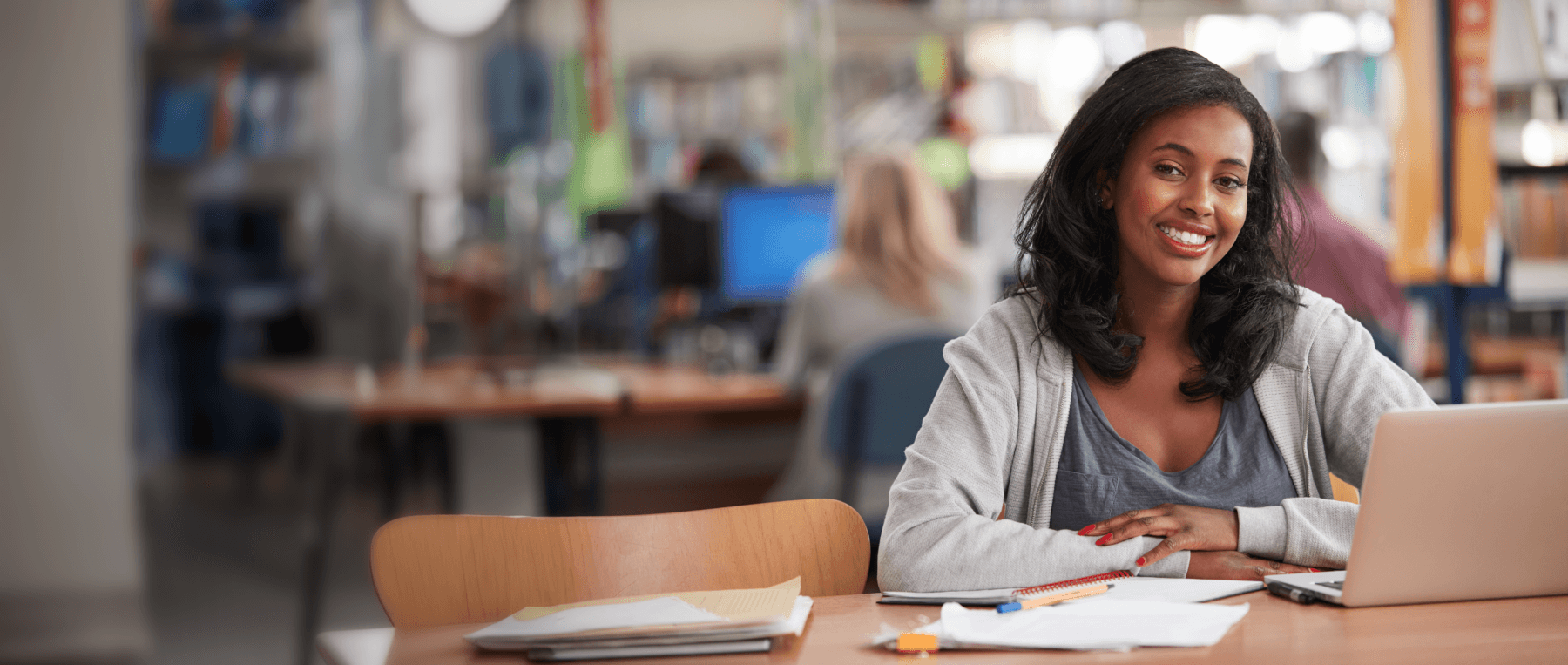 A young woman is in a library at a table with her laptop studying. 