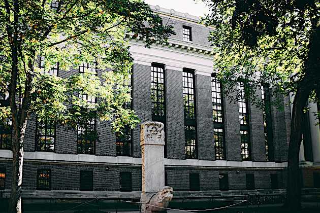 Exterior of a black brick building university building with a sculpture and bike rack out front. 