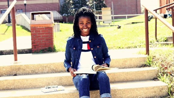 A girl is sitting outside on some steps smiling with an open notebook on her lap. 