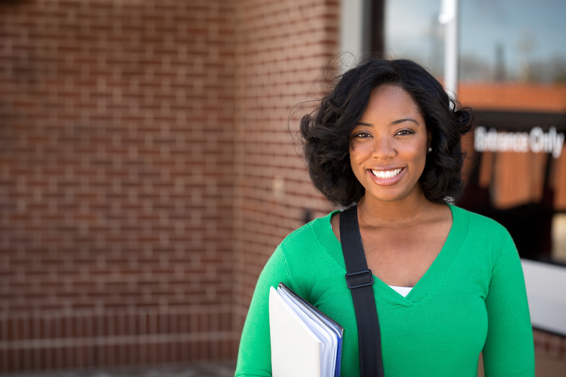 A female student with books and a bag is smiling at the camera. 